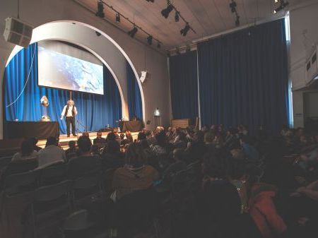A man presenting a science show on stage with a theatre audience