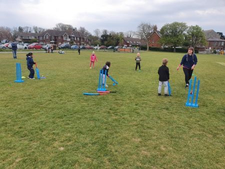 Small children and an instructor on grass playing cricket with soft bats and wickets