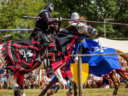 Two people jousting on horses, with an audience in the background.