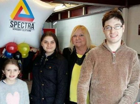 3 children and two adults holding a balloon with the Spectra Sensory Clothing logo on it.
