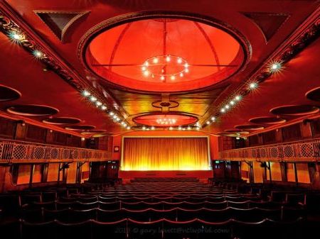 The Dome Cinema screen room with seats and stage. Red lighting projecting making the scenery a dark red, curtains on main stage shut.