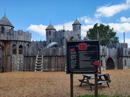 A photo of the Dragon Castle at Knockhatch. It is a wooden castle with lots of slides, stairs, rock climbing areas and entrances.