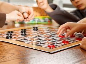 A close up of a draughts board with a game in progress with a group of people watching on
