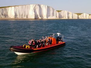 Red boat out in the sea with the white beachy head cliffs in the background. There are many people in the boat.