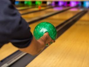 A person throwing a ball down the bowling alley