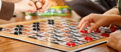 A close up of a draughts board with a game in progress with a group of people watching on