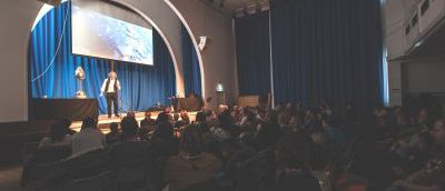 A man presenting a science show on stage with a theatre audience