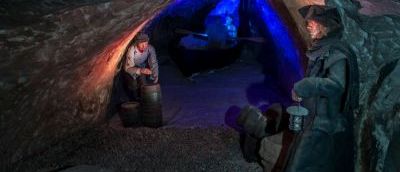 Two male wax figures in a cave near beer barrels