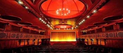 The Dome Cinema screen room with seats and stage. Red lighting projecting making the scenery a dark red, curtains on main stage shut.