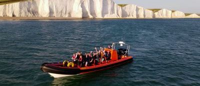 Red boat out in the sea with the white beachy head cliffs in the background. There are many people in the boat.