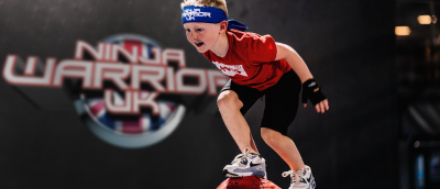 A little boy with a blue ninja warrior uk headband about to jump into a ball pit.